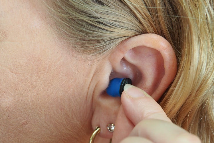 Woman inserts earplug into her ear.
