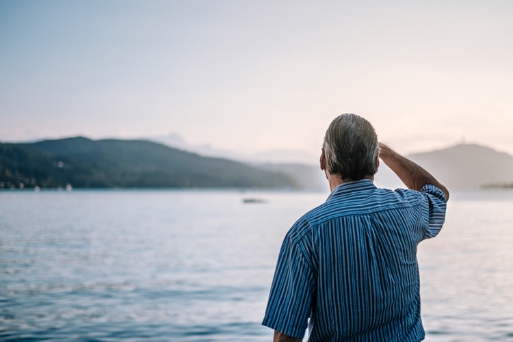 Older man staring out at a lake.