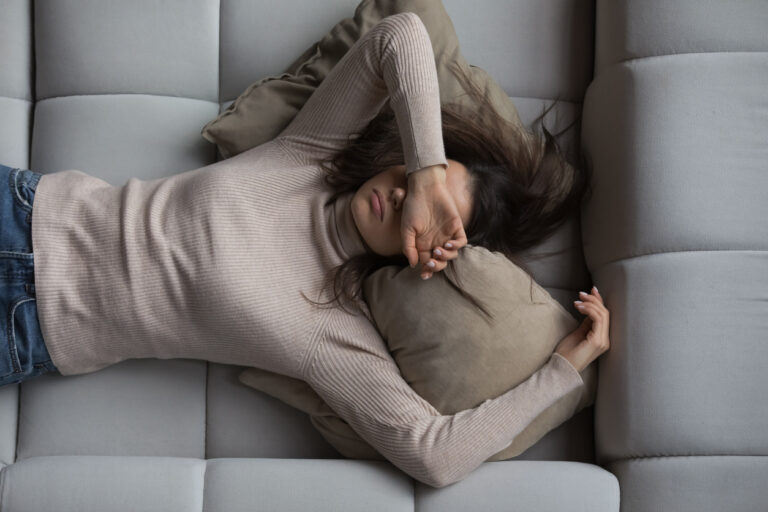 Tired woman laying on a couch with a hand over her face.